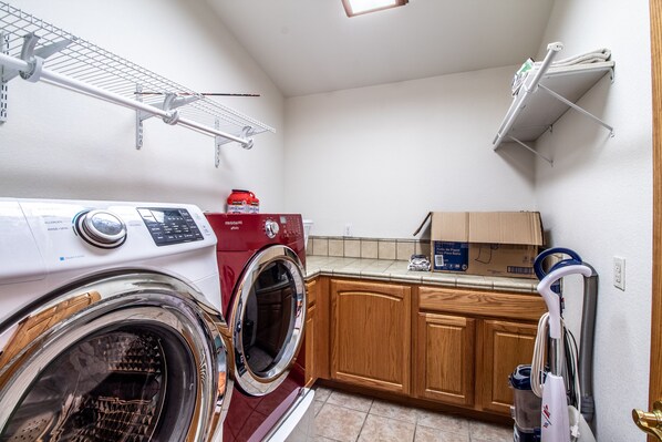 Une buanderie équipée d’un lave-linge et d’un sèche-linge à chargement frontal, de meubles en bois et d’une étagère avec une boîte.