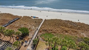 A beach with a wooden boardwalk, palm trees, and a view of the ocean. - Show-stopping views at this oceanfront condo w/indoor & outdoor pools, lazy river, kids' pool (North Myrtle Beach)