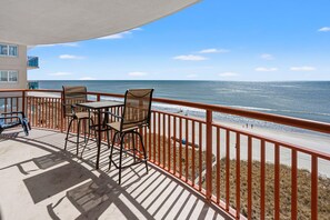 Een balkon met een tafel en stoelen, met uitzicht op een strand en de oceaan.
