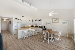 A modern kitchen with white cabinets, a wooden island with bar stools, a dining table with chairs, and a ceiling fan. - Beachfront Condo! West End PCB - Steps to the beach! Harbor Arms #6 - Dog Friendly (Panama City Beach)