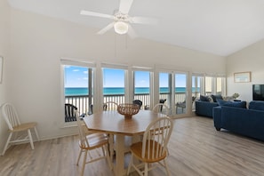 Relax in this spacious living area with a high ceiling, featuring a dining table, sofa, and TV, with ocean views through large windows.
