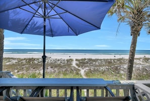 A beach view with a wooden deck and a blue umbrella.