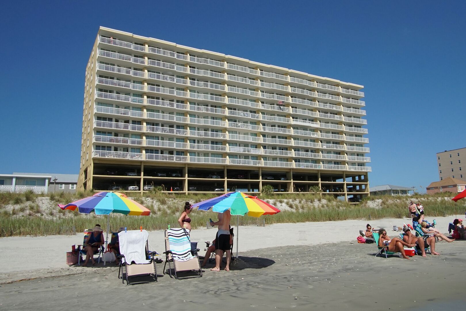 Et hotel ved stranden med flere etager, udendørs siddepladser og parasoller.