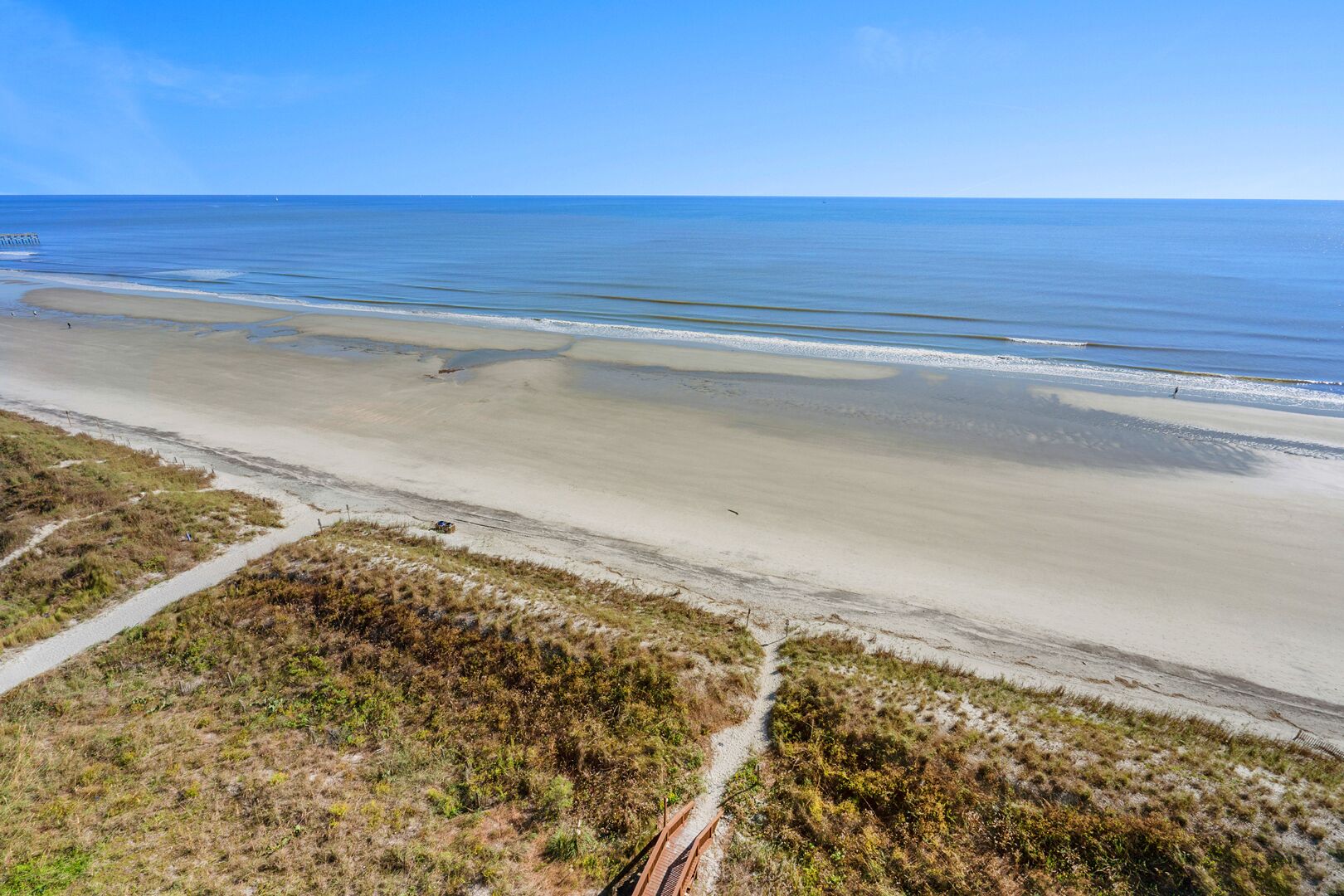 Ett kustlandskap med en sandstrand, en klar himmel och en järnvägsräls som leder ut mot havet.