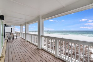 Eine überdachte Holzterrasse mit weißen Geländern, einer Sitzgelegenheit und Blick auf Strand und Meer.