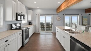 A modern kitchen with white cabinets, stainless steel appliances, and a wooden ceiling beam.