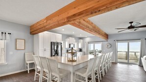 A spacious kitchen with white cabinets, a large island with chairs, and a view to the outside.