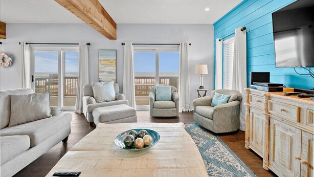 A spacious living room with a large window, a ceiling fan, and a TV mounted on the wall.