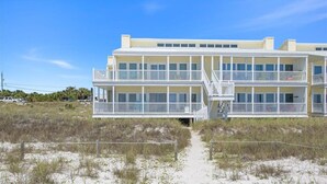 Een meerlaags hotel aan het strand met balkons, een zandstrand ervoor en een heldere lucht.