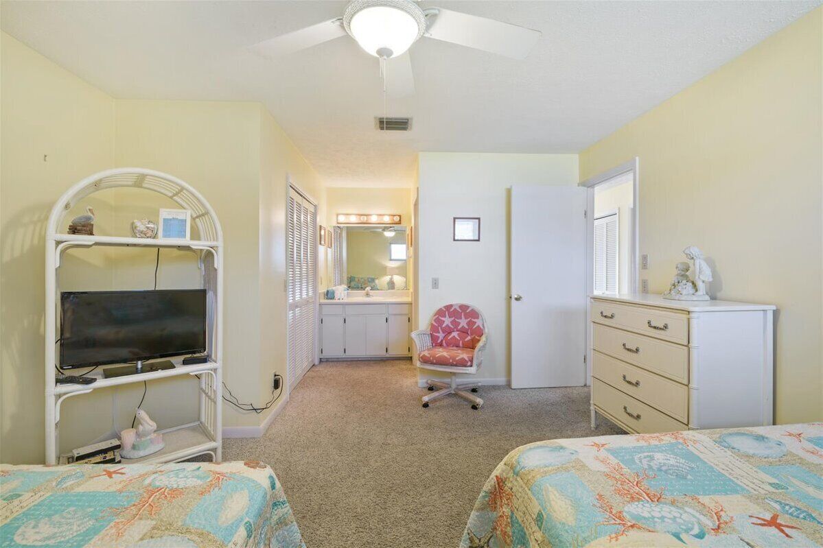 Une chambre avec deux lits, un bureau avec une télévision, une chaise, une commode et une salle de bain visible à travers une porte ouverte.