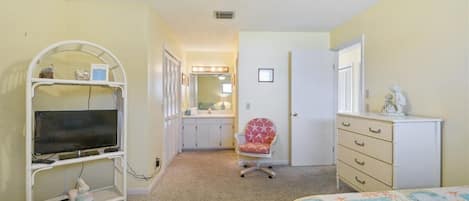 Une chambre avec deux lits, un bureau avec une télévision, une chaise, une commode et une salle de bain visible à travers une porte ouverte.