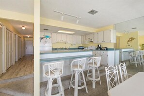 Een keuken met witte kasten, een bar met witte rieten stoelen, en een eettafel met stoelen.