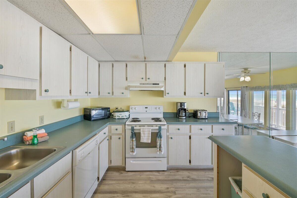 A kitchen with white cabinets, a stove, a sink, and a window with blinds.