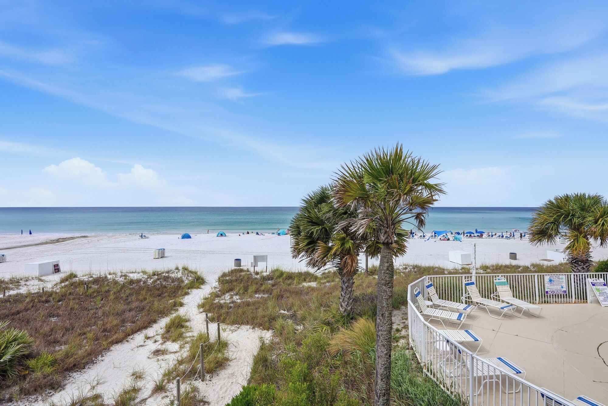 A beach with white sand, palm trees, and a clear blue sky.