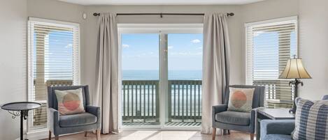 A room with two armchairs, a sofa, a small table, and a lamp. There is a view of the ocean through a glass door.