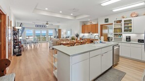 A modern kitchen with white cabinets, a central island, and a view to the ocean.