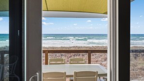 A view of the ocean from a covered outdoor seating area with a table and chairs.