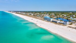 An aerial view of a coastal area with a beach, a large hotel with multiple buildings, and a body of water.