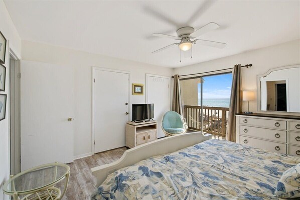 Un dormitorio con cama, ventilador de techo, televisor, silla, cómoda y balcón con vistas.