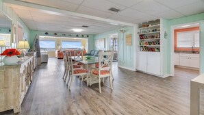 A spacious room with a large dining table, chairs, and a view to the outside.