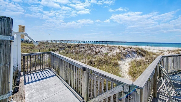 A wooden boardwalk leading to a beach with a pier in the distance.