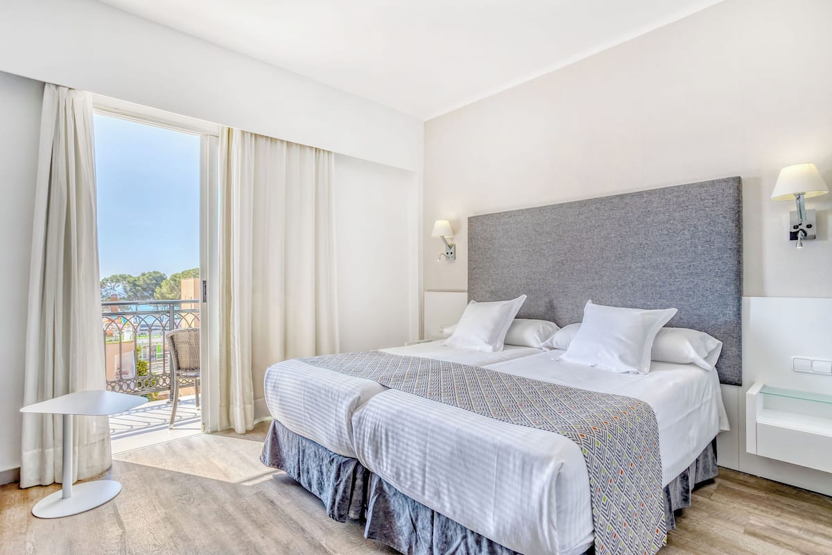 A hotel room with a large bed, a balcony, a small table, and a modern headboard.