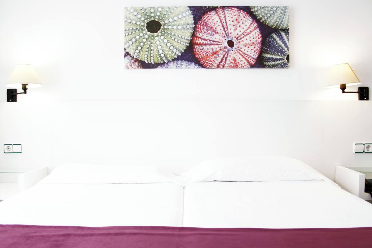 A hotel room with a bed, two bedside lamps, a wall-mounted artwork, and a nightstand.