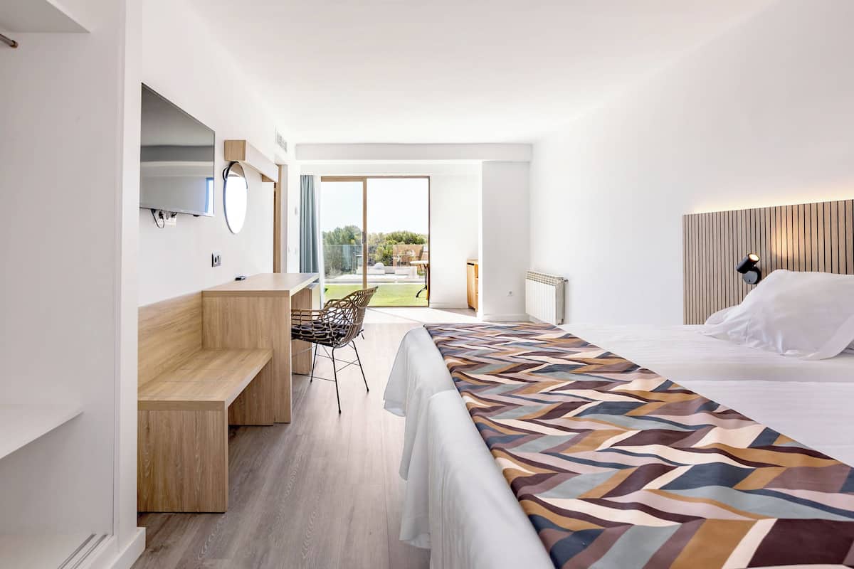 A modern hotel room with a bed, a desk, a chair, and a large window.