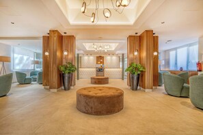 A spacious lobby with a central round ottoman, wooden accent walls, and a reception desk in the background. - Hotel Morlans Garden (Calvia)