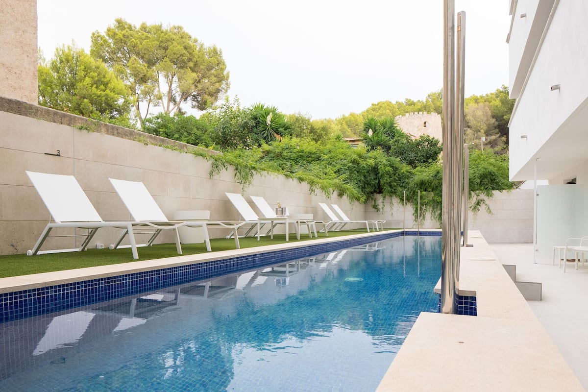 A swimming pool with clear blue water, surrounded by white lounge chairs and a modern building.