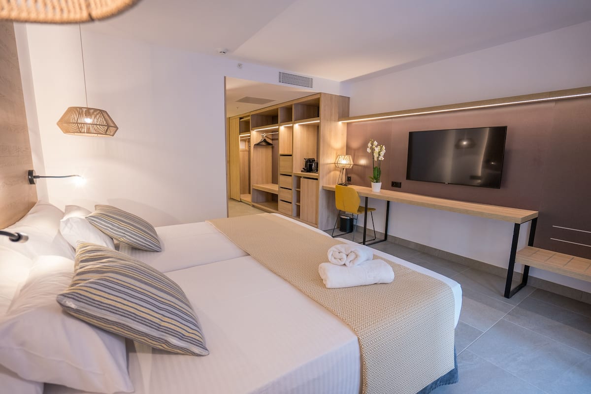 A modern hotel room with a neatly made bed, a TV mounted on the wall, and a walk-in closet.