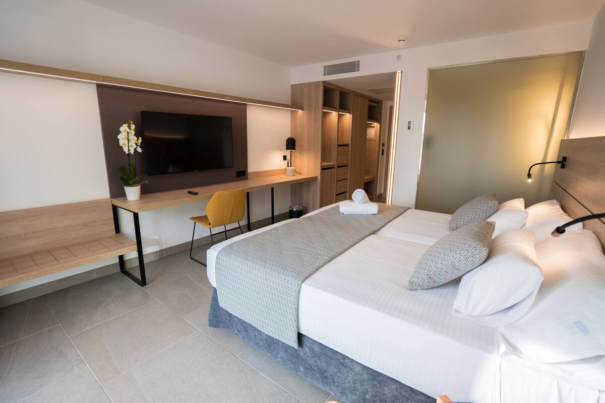 A modern hotel room with a large bed, a desk with a chair, a flat-screen TV, and a walk-in closet.