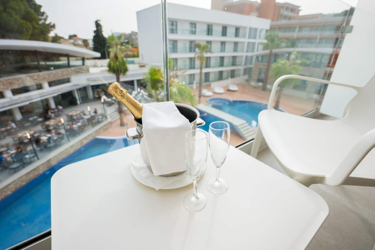 A table with a bottle of champagne and two glasses, overlooking a pool and outdoor seating area.