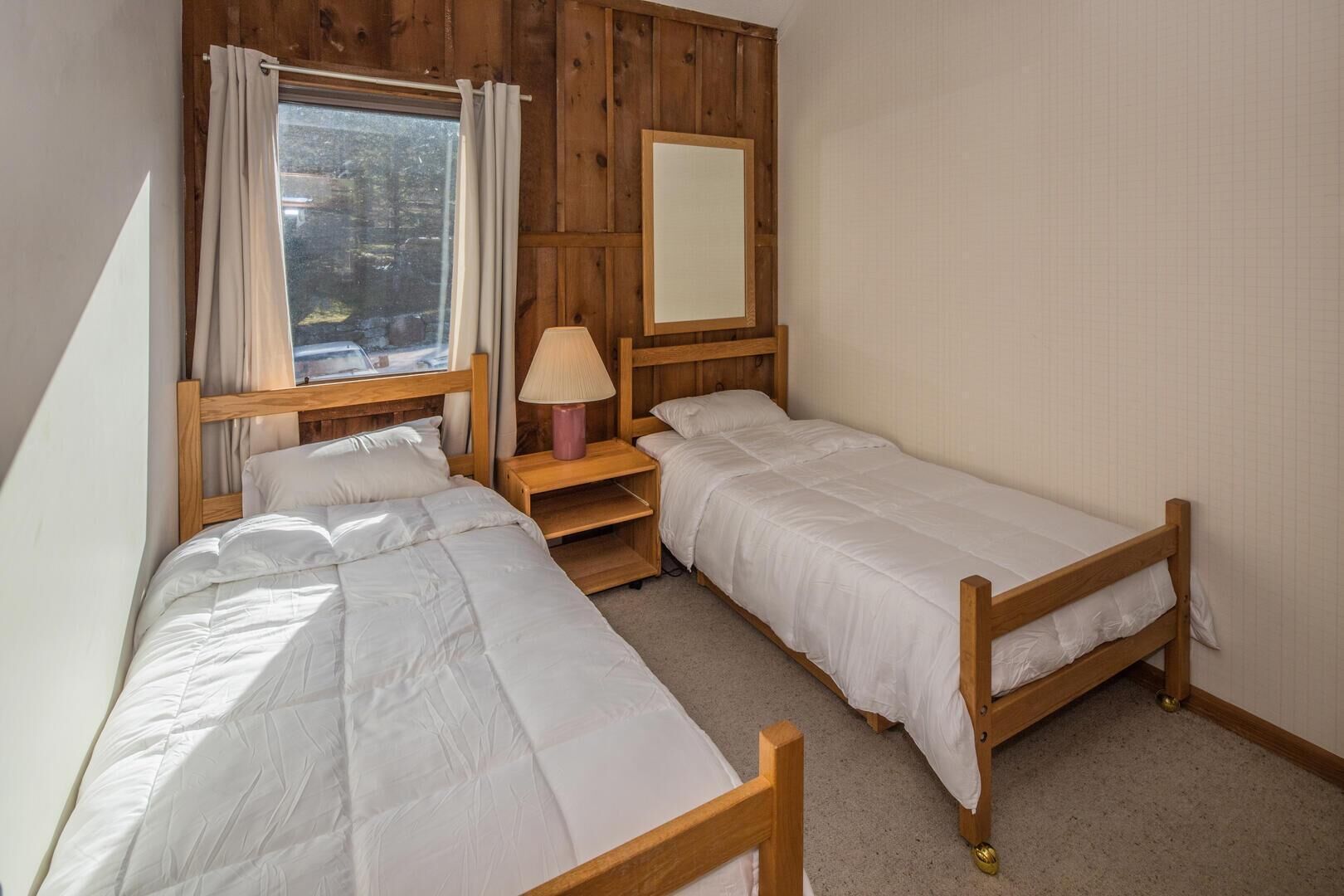 A room with two wooden bunk beds, a window with curtains, a bedside lamp, and a mirror on the wall.