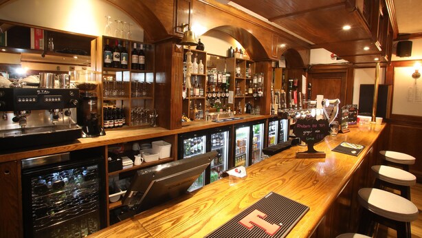 A bar with wooden shelves stocked with bottles and glasses, a coffee machine, and a cash register. - The Royal Hotel Stromness (Stromness)