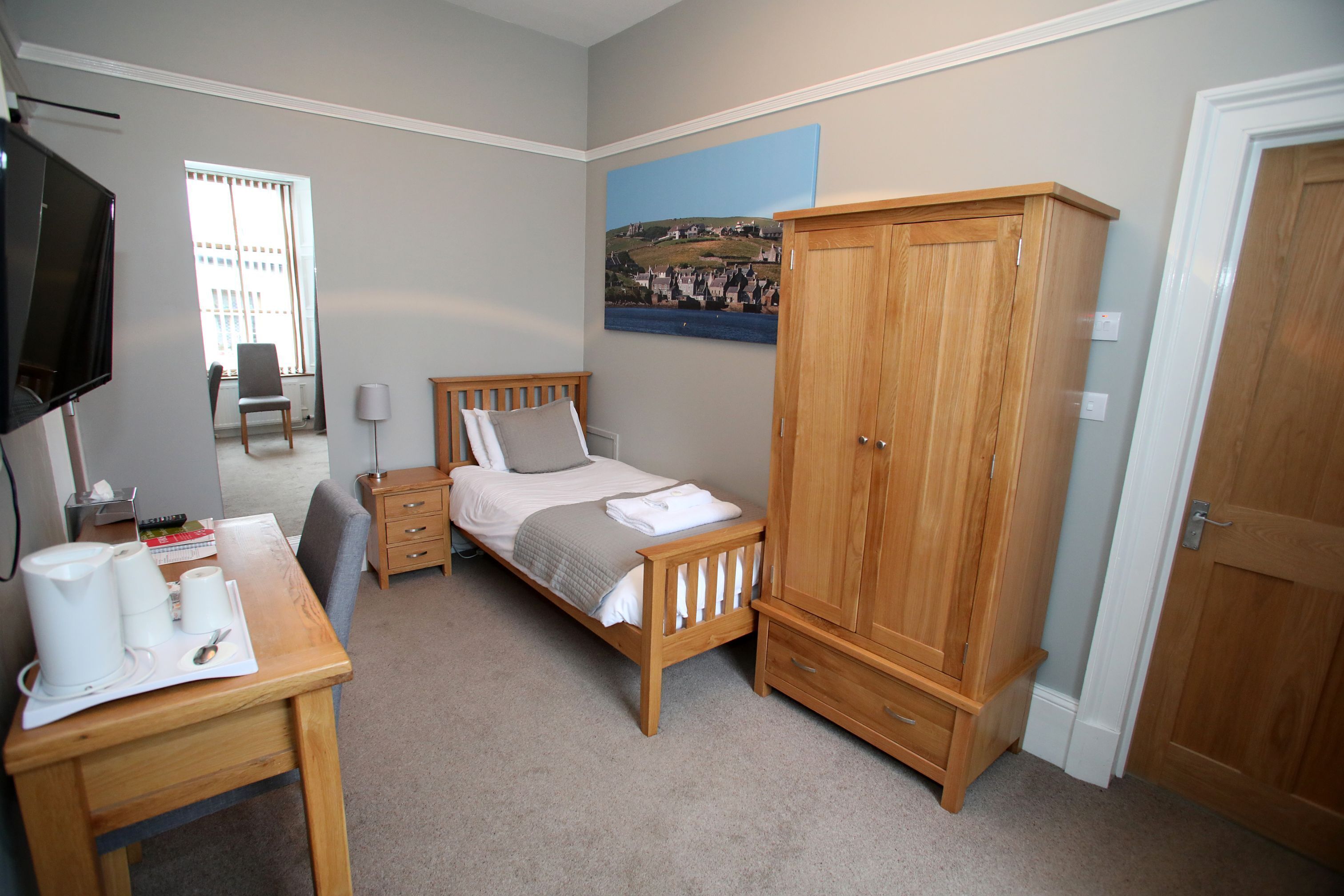 A bedroom with a bed, wooden wardrobe, bedside table with cups, and a TV.