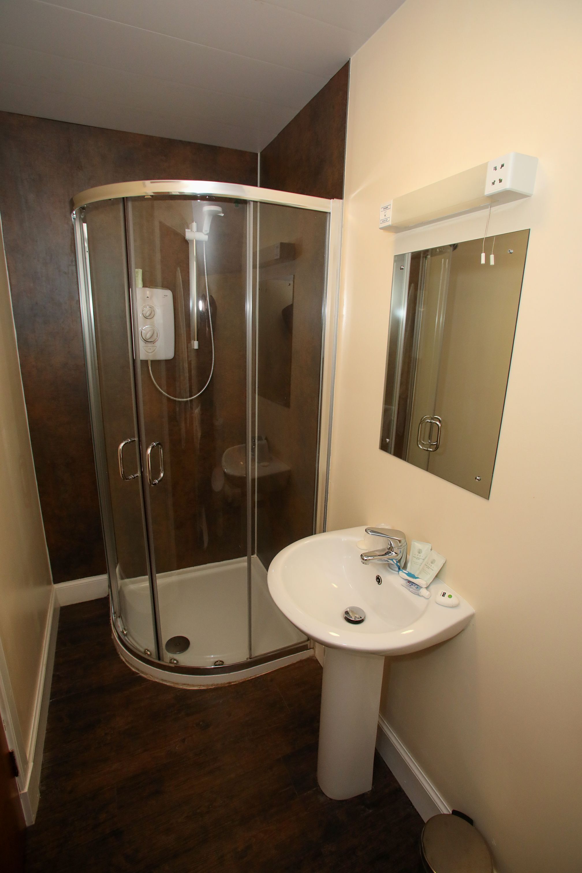 A bathroom with a glass shower enclosure, a pedestal sink, and a mirror above the sink.
