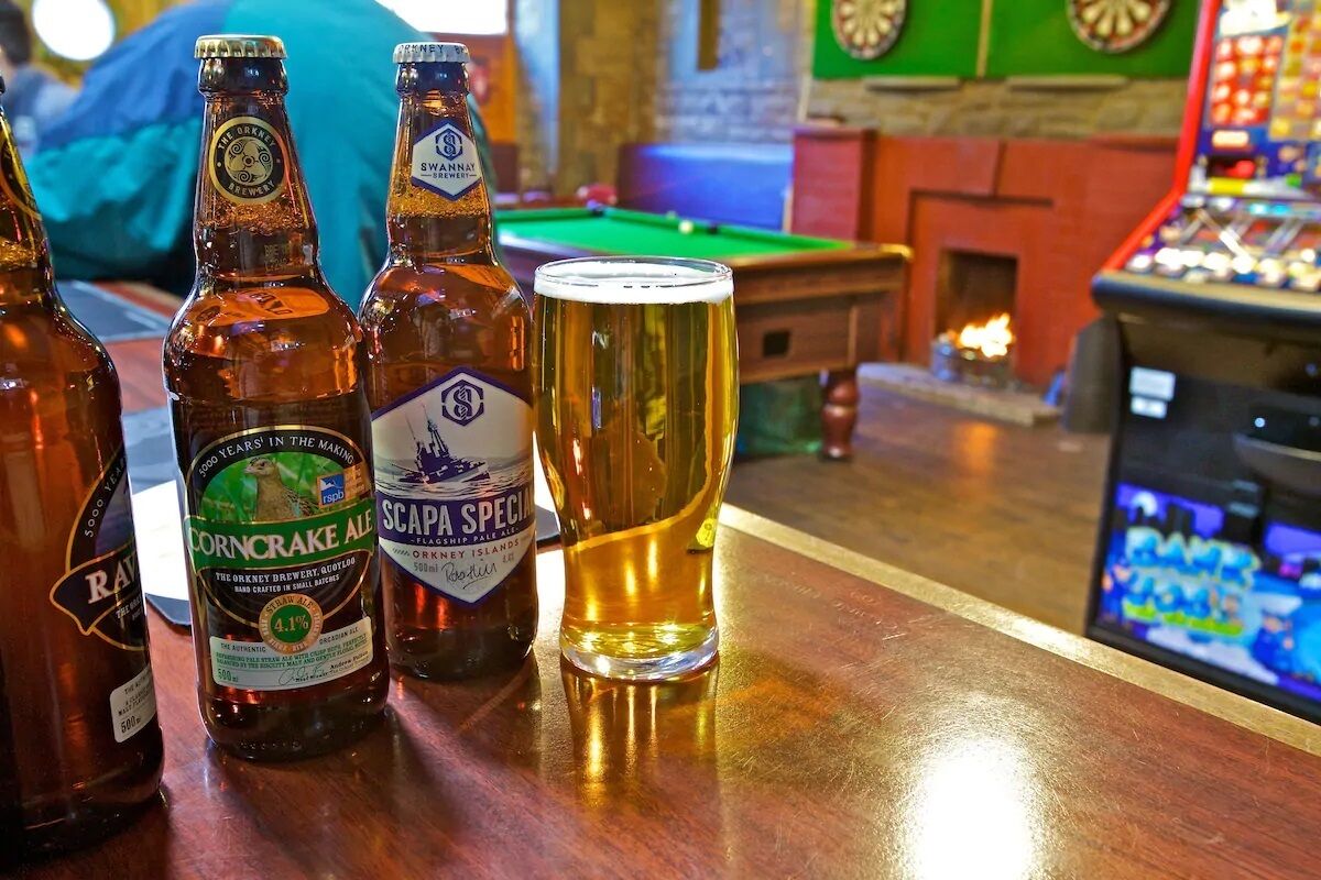 Tres botellas de cerveza y un vaso sobre la barra de un pub.