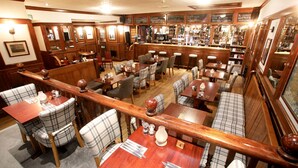 A bar area with wooden furniture, bar stools, and a variety of bottles and glasses on shelves. - The Royal Hotel Stromness (Stromness)