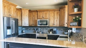A modern kitchen with wooden cabinets, stainless steel appliances, and a central island with bar stools. - 4 bedrooms 3 bath close to downtown and RMNP- beautiful! (Estes Park)