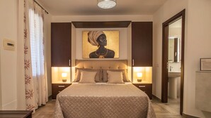 A hotel room with a large bed, bedside lamps, a painting on the wall, and a wooden floor. - Il Corallo - Bilo 2 IV (Lampedusa)