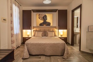 A hotel room with a large bed, bedside lamps, a painting on the wall, and a wooden floor. - Il Corallo - Bilo 2 IV (Lampedusa)
