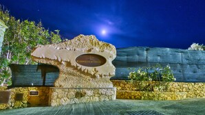 A stone sculpture with a plaque reading "IL CORALLO RESIDENCE" in front of a stone wall and a wooden fence under a night sky. - Il Corallo - Bilo 2 IV (Lampedusa)