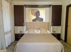 A bedroom with a bed, a headboard, bedside tables, and a painting on the wall. - Il Corallo - Bilo 2 IV (Lampedusa)