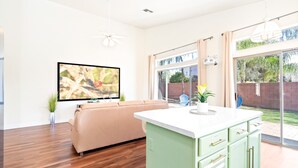 A modern kitchen with a green island, a beige sofa, and a large window overlooking a backyard. - Catalina Serenity Paradise 4 Bed 2 Bath (Tucson)