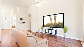 A spacious living room with a large flat-screen TV, a leather sofa, a ceiling fan, and a minimalist decor. - Catalina Serenity Paradise 4 Bed 2 Bath (Tucson)