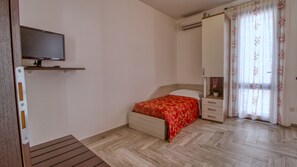 A bedroom with a bed, a TV, a wardrobe, a bedside table, and a window with curtains. - Il Corallo - Bilo 3 II (Lampedusa)