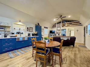 A modern kitchen with blue cabinets, a dining area with wooden chairs, and a loft bedroom with a sloped ceiling. - Peaceful Hill Country Cabin - Family & Dog - Friendly with Stunning Night Skies (Harper)