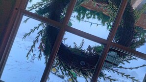 Een raam met uitzicht op een besneeuwd landschap, inclusief een krans en een kerstboom.