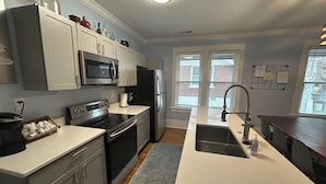 A modern kitchen with stainless steel appliances, a central island with a sink, and a view of the outside through large windows.